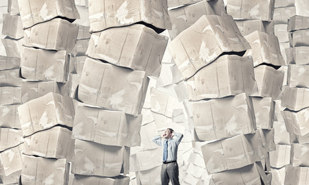 Young businessman and stack of carton boxes behind himの写真素材