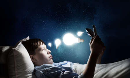 Teenage boy in pajamas lying in bed using tablet pcの写真素材