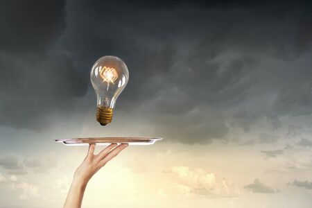 Hand holding tray with glowing light bulbの写真素材