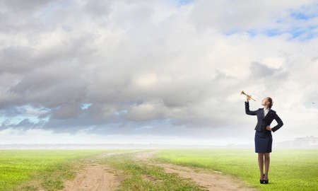 Young pretty businesswoman playing melody on trumpetの写真素材