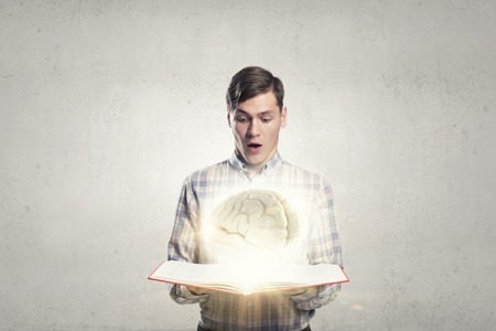 Shocked man holding opened book with brain pictureの写真素材