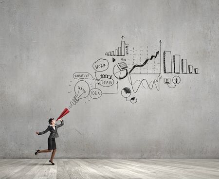 Young woman in suit and bowler hat screaming in paper trumpetの写真素材