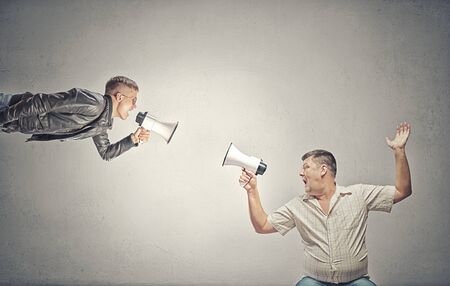 Young man and elder one screaming aggressively in megaphone on each otherの写真素材