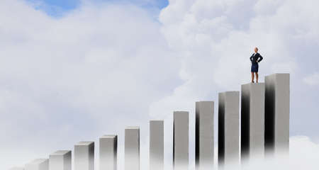 Businesswoman with hands on waist standing on graph barの写真素材