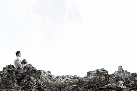 Young thoughtful businessman sitting alone on rock top
