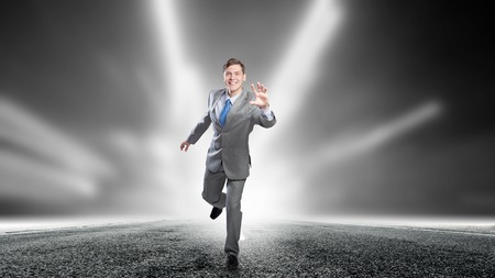 Young businessman in suit running on asphalt roadの写真素材