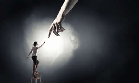 Young woman standing on chair and reaching hand to get helpの写真素材
