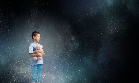 Cute little boy with toy bear in night darknessの写真素材