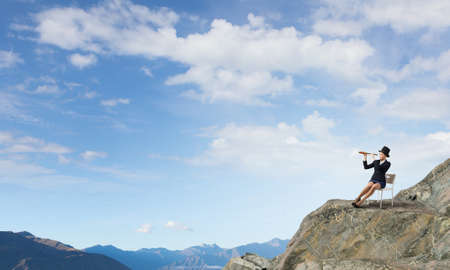 Pretty girl wearing retro hat siting on chair and looking in spyglassの写真素材