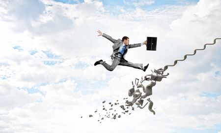 Young businessman walking up collapsing staircase representing success conceptの写真素材