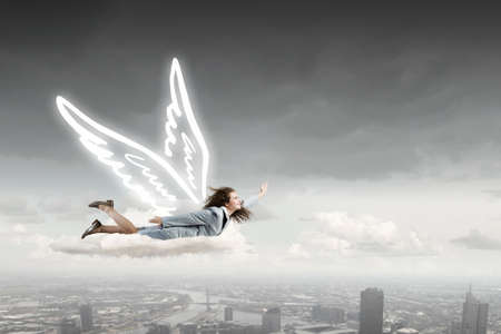 Young businesswoman with drawn wings flying high in skyの写真素材