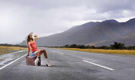 Traveler woman sits on retro suitcase and waiting for carの写真素材