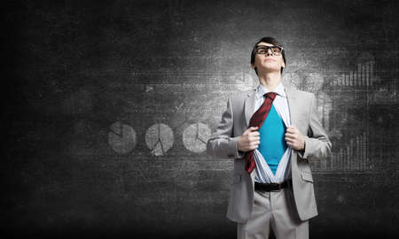 Young businessman acting like super hero and tearing his shirt offの写真素材