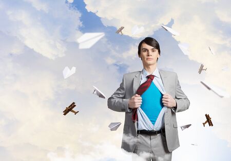 Young businessman acting like super hero and tearing his shirt offの写真素材