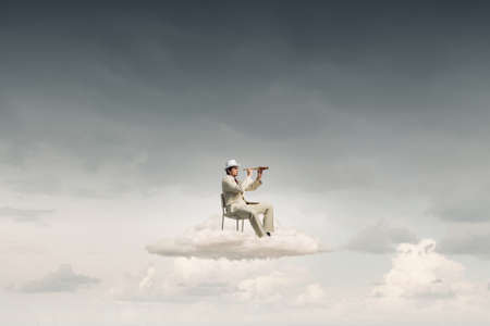 Businessman in white suit and hat sitting in chair and looking in spyglassの写真素材