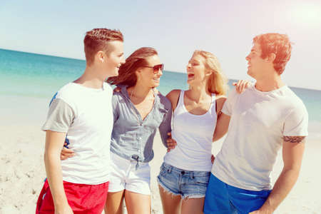Company of young friends on the beach walking along the shore