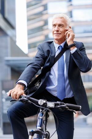 Successful businessman on bicycle in city holding mobile phoneの写真素材