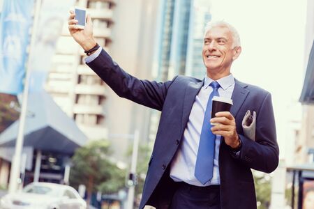 Businessman in suit catching taxi in city with cup of coffee in his handsの写真素材