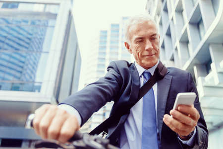 Successful businessman in suit riding bicycle and holding mobile phoneの写真素材