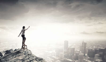 Businesswoman standing on chair and reaching hand to touch somethingの写真素材