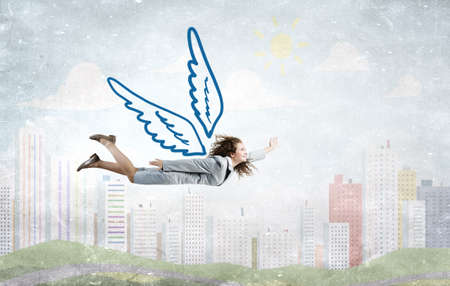 Young businesswoman with drawn wings flying high in skyの写真素材