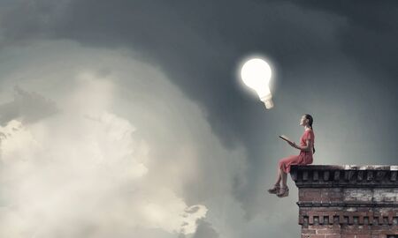 Young attractive woman sitting on top of building and reading bookの写真素材