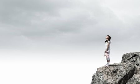 Cute girl wearing pajamas with toy bear in hand standing on rock edgeの写真素材