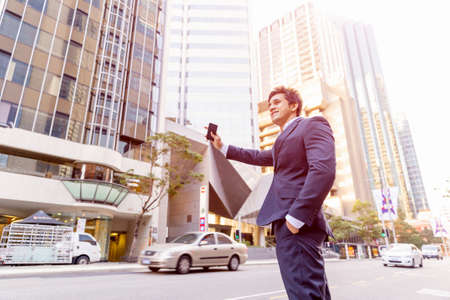 Businessman in suit catching taxi in city with mobile phone in his handsの写真素材