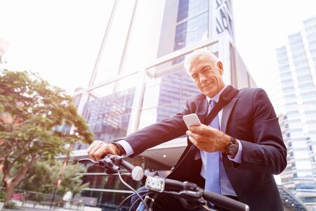 Successful businessman in suit riding bicycle and holding mobile phone