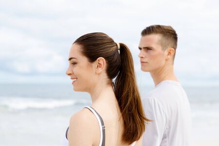 Young couple looking thoughtful while standing next to each other on beach in sports wear