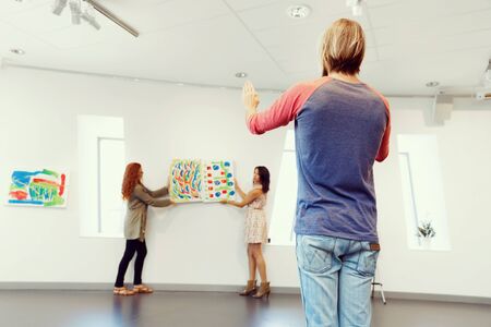 Young artists in gallery hanging together painting on wallsの写真素材