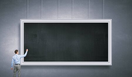 Businessman standing with back and drawing on blank chalkboardの写真素材