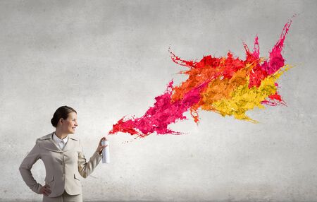 Young businesswoman spraying colorful paint from balloonの写真素材