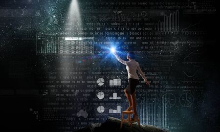 Back view of businesswoman standing on chair and reaching infographs on wallの写真素材