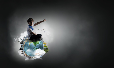 Cute school boy sitting on Earth planet and pointing with finger up.  の写真素材