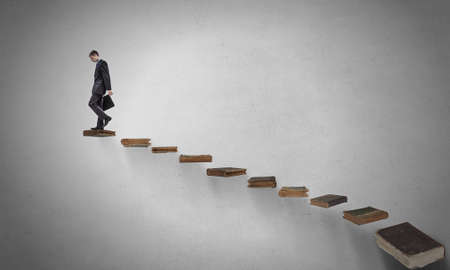 Businessman walking on career ladder made of booksの写真素材
