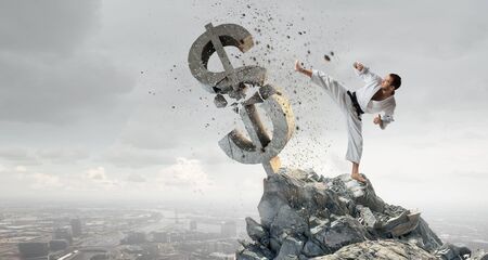 Young determined karate man breaking with leg concrete dollar signの写真素材