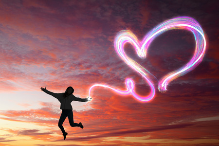 Young girl jumping high in sky and drawing love signの写真素材