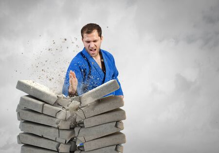 Young determined karate man breaking with hand concrete bricksの写真素材
