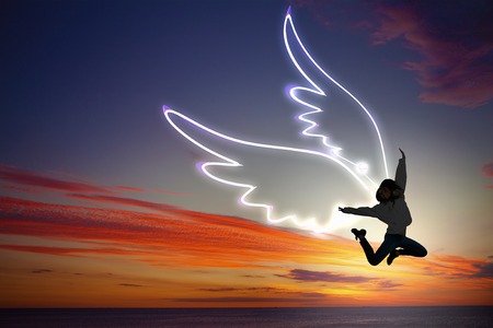 Young girl with drawn wings jumping high in skyの写真素材