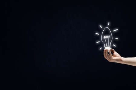 Male hand on dark background showing drawn light bulbの写真素材