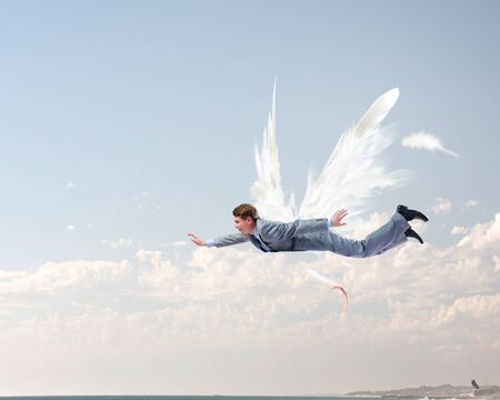 Young businessman with drawn wings flying in skyの写真素材