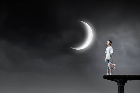 Cute little boy with toy bear in night darknessの写真素材