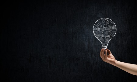 Male hand on dark background showing drawn light bulbの写真素材