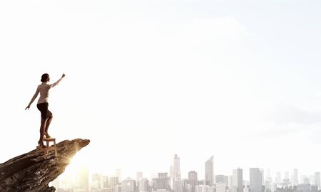 Businesswoman standing on chair and reaching hand to touch somethingの写真素材
