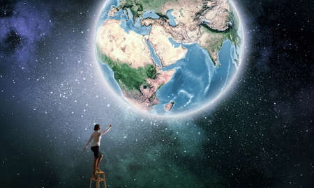 Businesswoman standing on chair and reaching Earth planet. の写真素材