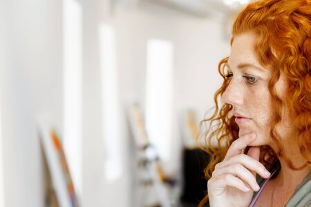 Young caucasian woman in an art gallery in front of painting displayed on white wallの写真素材