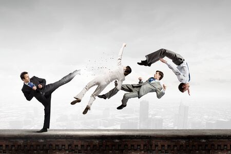 Young determined karate businessman fighting with team of businesspeople