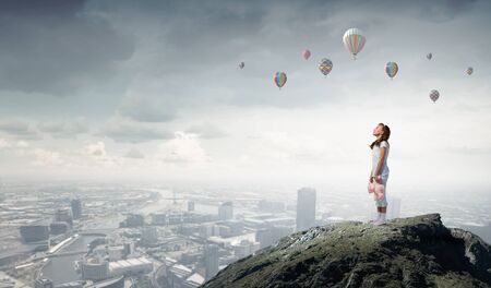 Cute girl wearing pajamas with toy bear in hand standing on rock edgeの写真素材