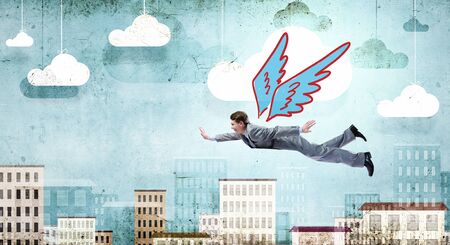 Young businessman with drawn wings flying in skyの写真素材